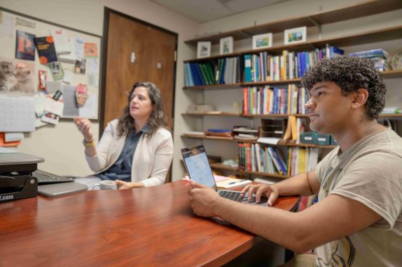 A student has a computer in front of them and is collaborating with a professor.