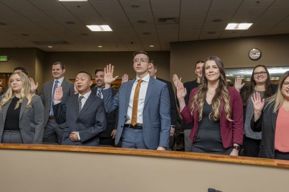 Students in a courtroom getting sworn-in with right hand raised.