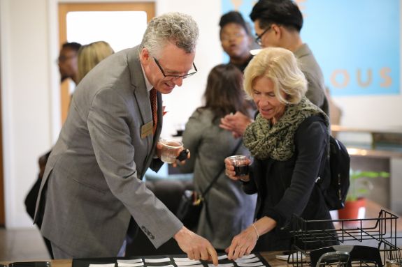 a man in a grey suit helps a woman with finding a name tag.