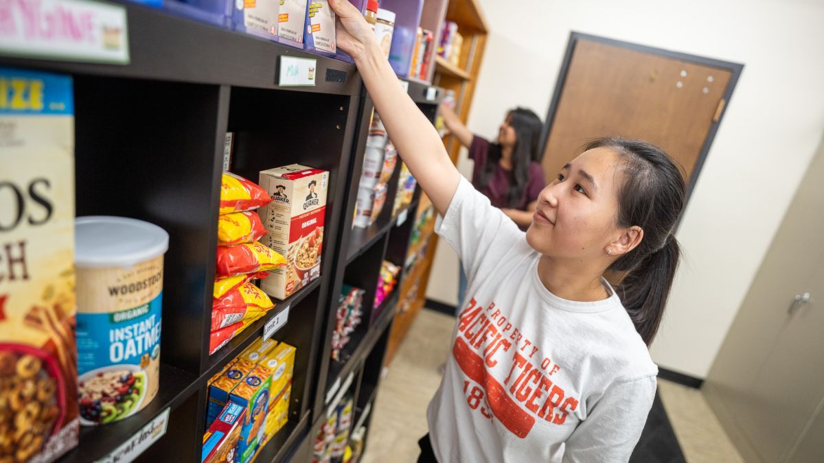 A student restocks shelves at the Pacific Food Pantry