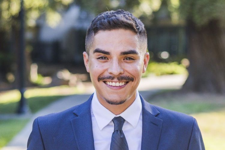 A man in a suit standing outside and smiling.