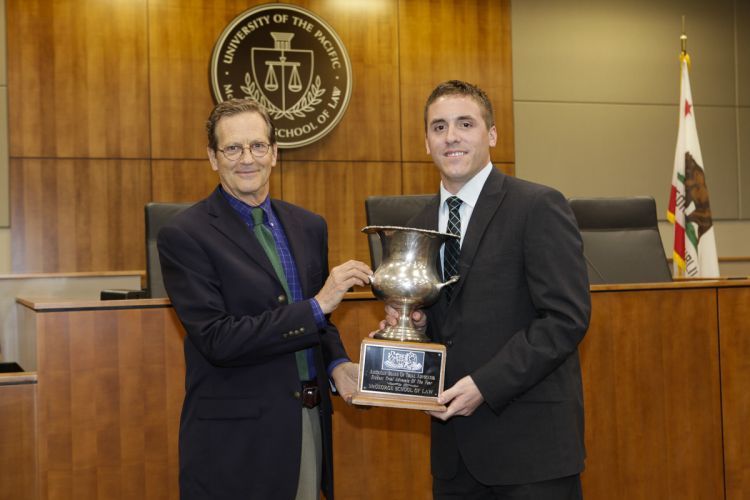 Two men in suits hold a trophy