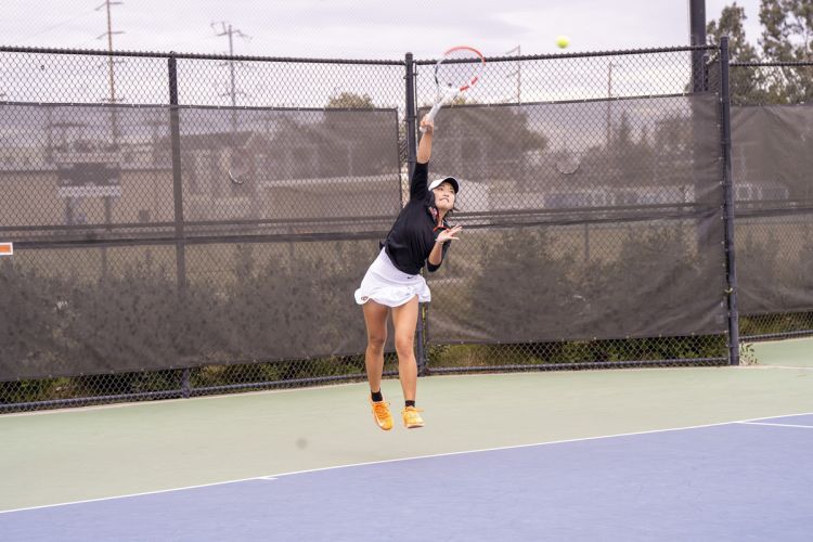 A student serves a ball on a tennis court