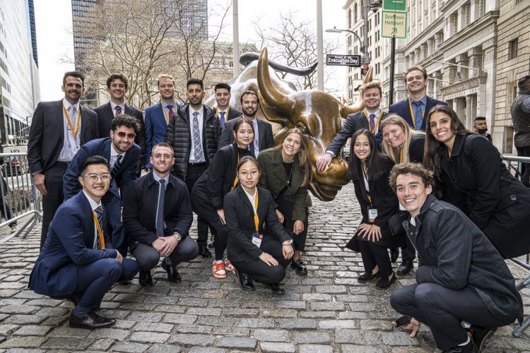 students stand next to the bull of Wall Street statue