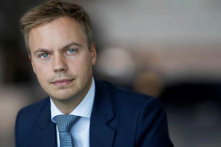 A man in a suit poses for a photo in front of a blurred background