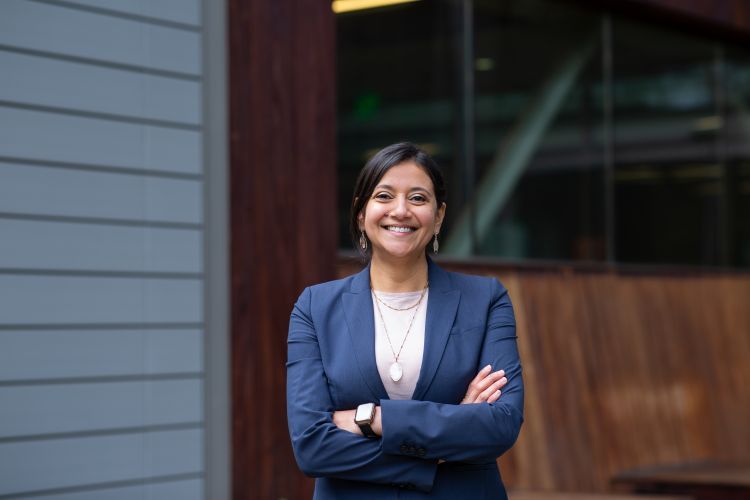 A woman in a navy suit poses smiling, with her arms crossed.