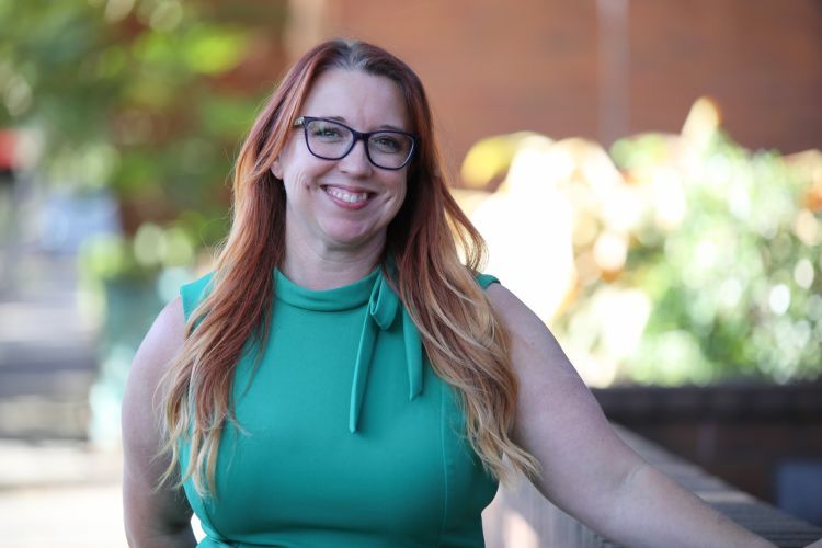 A red-haired woman in a green dress smiles for a photo while leaning on a railing 