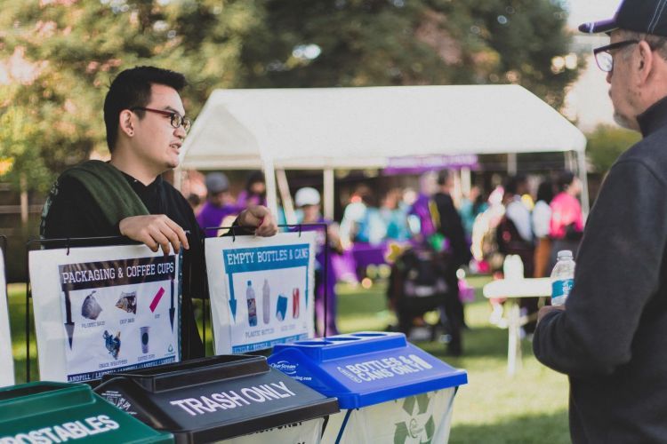 A student stands behind 3 bins used to sort waste 