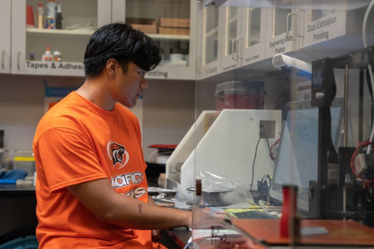 student stands at a 3D printer