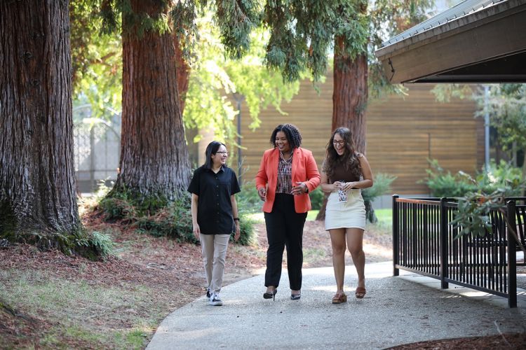 Three women walk on campus and talk to one another