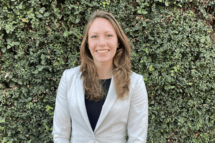 A woman in a suit poses for a photo in front of a wall of greenery