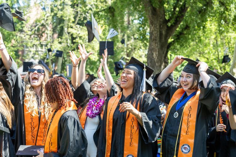 student-athletes throw their graduation caps into the air at commencement