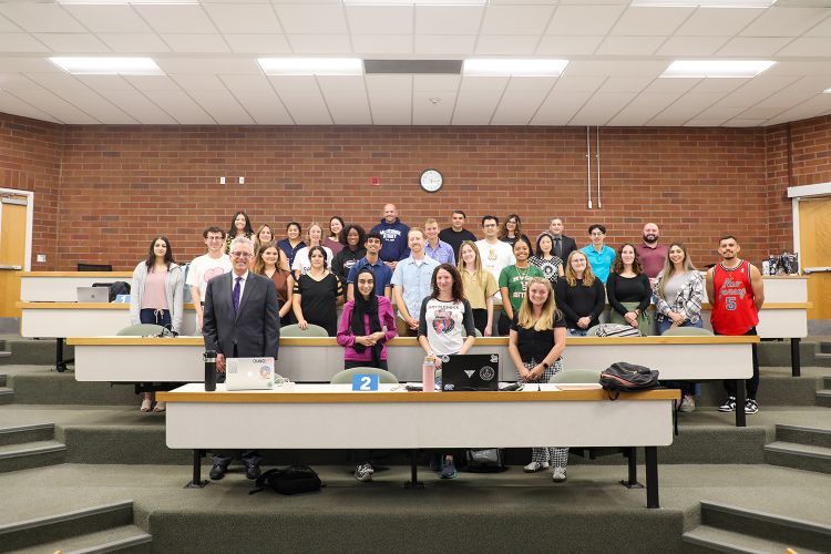 A professor poses with students in his class inside of a classroom