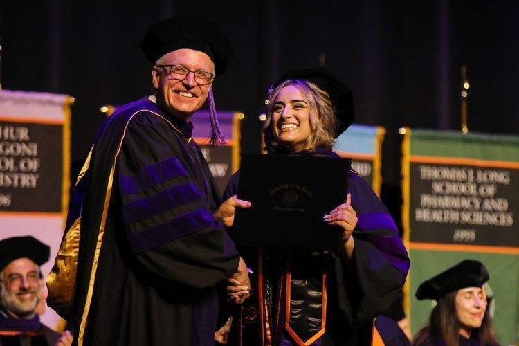 Two people hold a diploma at a graduation ceremony