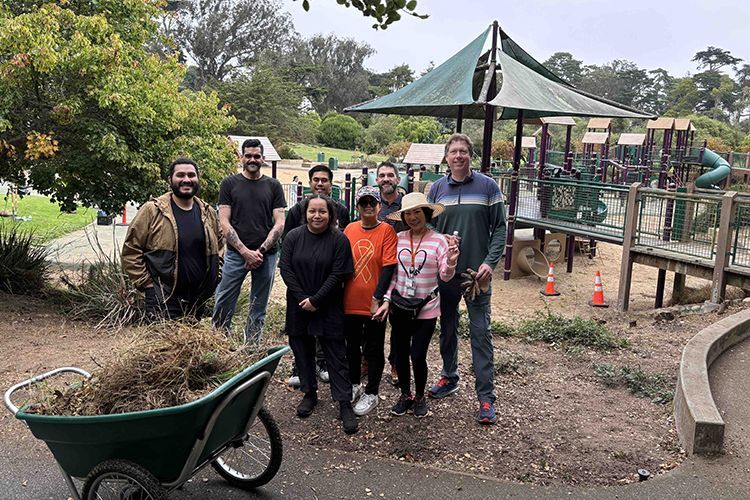 8 men and women with a wheel barrow of weeded dry grass at Koret's Playground in San Francisco