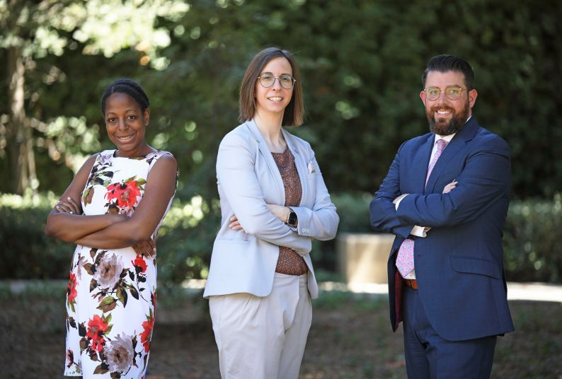 Three law professors pose for a photo in front of a green background.