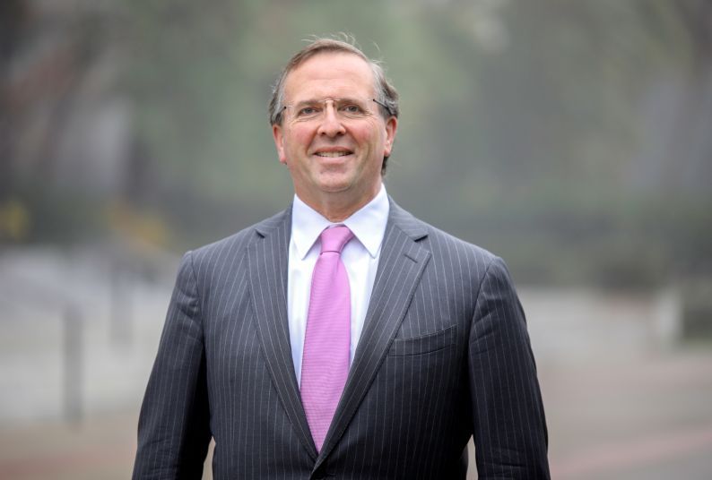 A portrait of Chris Micheli in a pinstripe suit and a pink tie.