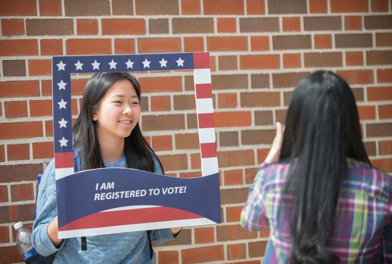 A student holds a sign reading "I am registered to vote" while someone takes a picture