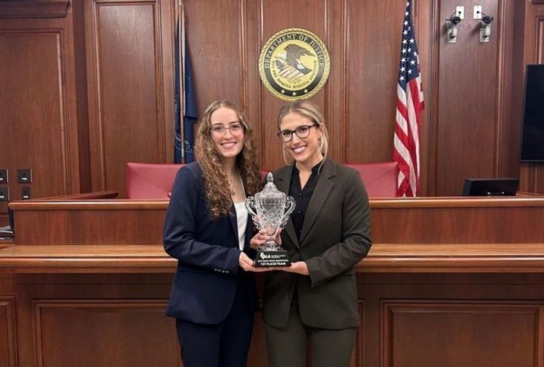 two students stand in a courtroom holding a trophy