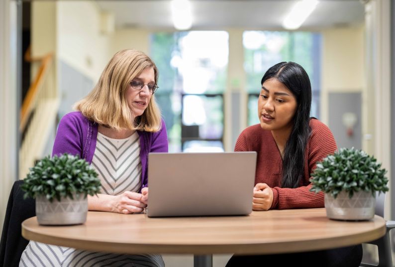 two people sitting at a table looking at a computer