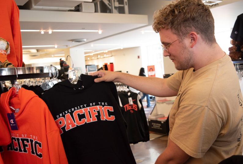 an alumni holds a black sweatshirt that reads University of the Pacific