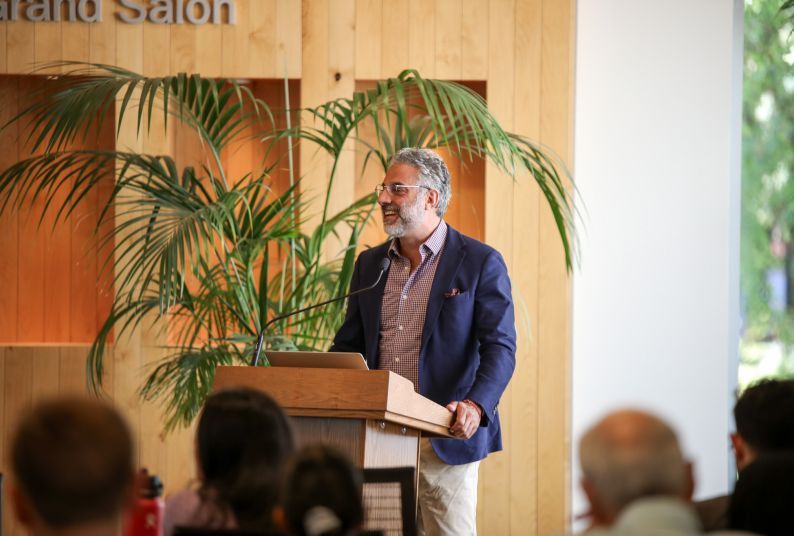 A male professor at a podium speaks to a crowd