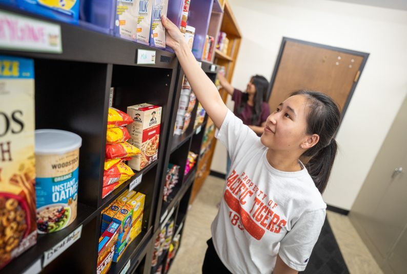 A student restocks shelves at the Pacific Food Pantry