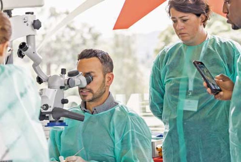 doctor looking into microscope with person behind him