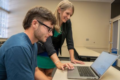 A student and professor look at a computer on a desk.