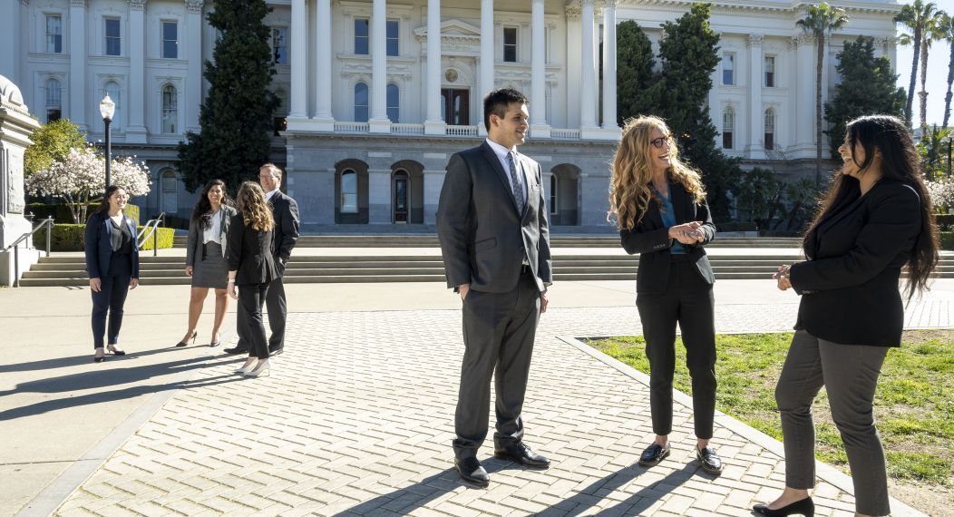 Two small groups of people in suits chat with each other in front of the Capitol Building 