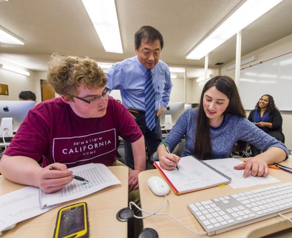 students working at a table with a faculty member helping